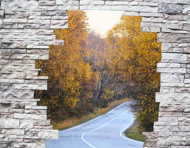 Twisting road among yellow trees in a window behind a stone wall, stock photo