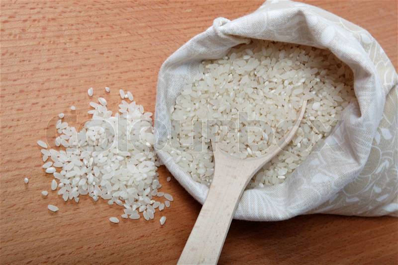 Rice in a bag and a spoon on a wooden table, stock photo