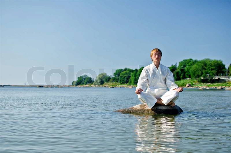 Man in kimono meditating on the rock in the sea, stock photo