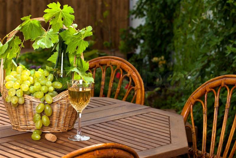 White wine bottle and bunch of grapes on basket, glass with in summer garden, stock photo