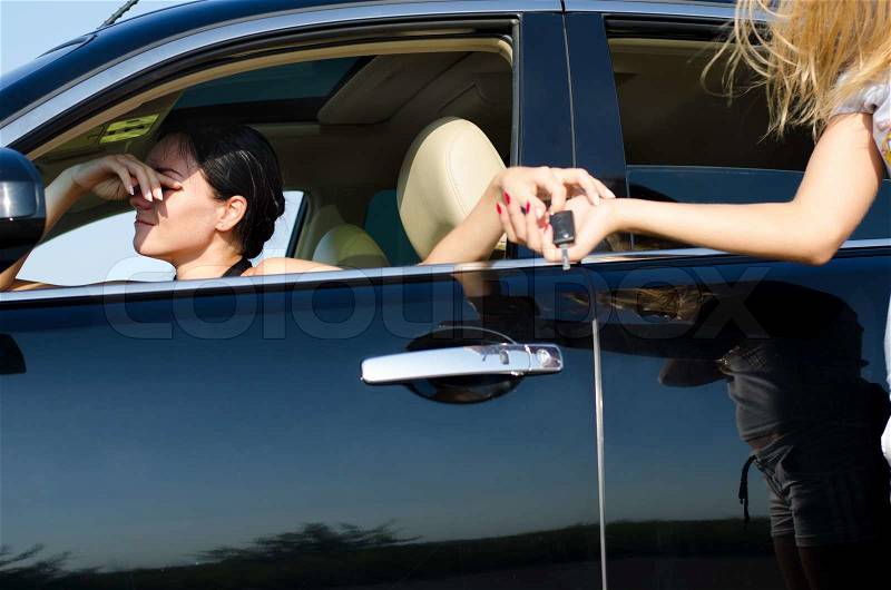 Tired woman driver with her hand to her head handing over her car keys to a second woman to take over, stock photo
