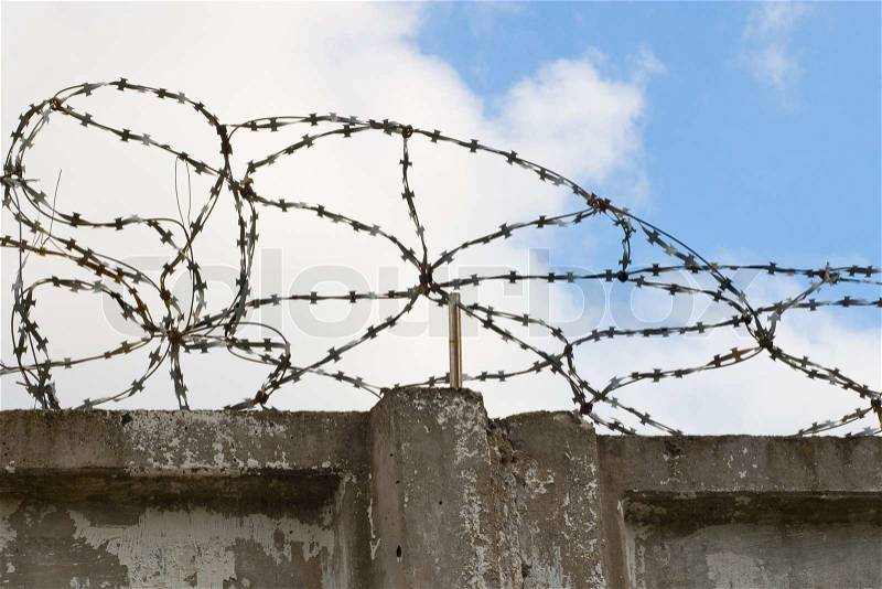 Stone wall with barbed wire against blue sky, stock photo