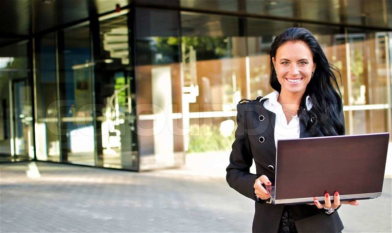 Businesswoman with notebook in front of office building, stock photo