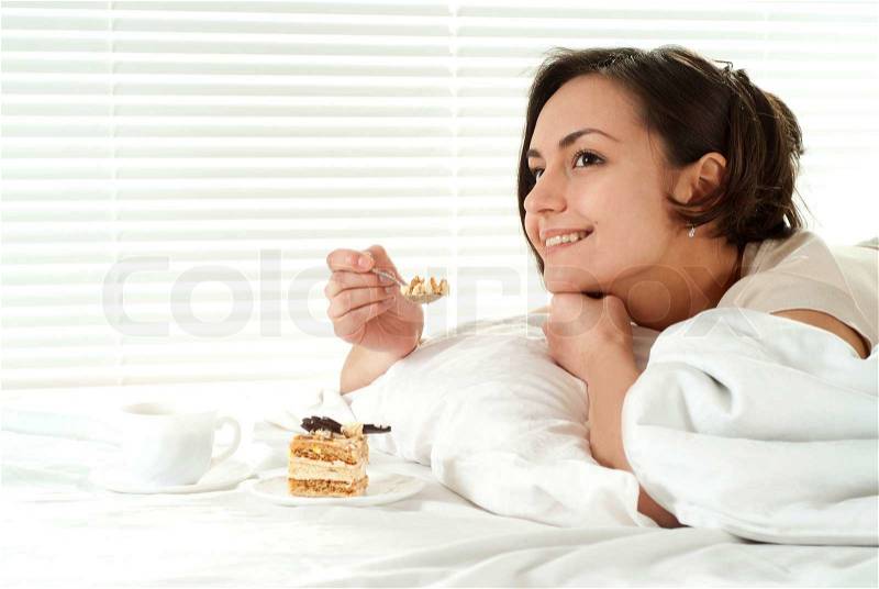 Nice Caucasian woman lying on a bed with a cake, stock photo