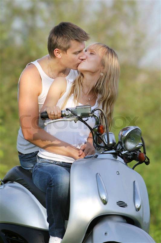 Young loving couple on motorbike / scooter on natural background, stock photo