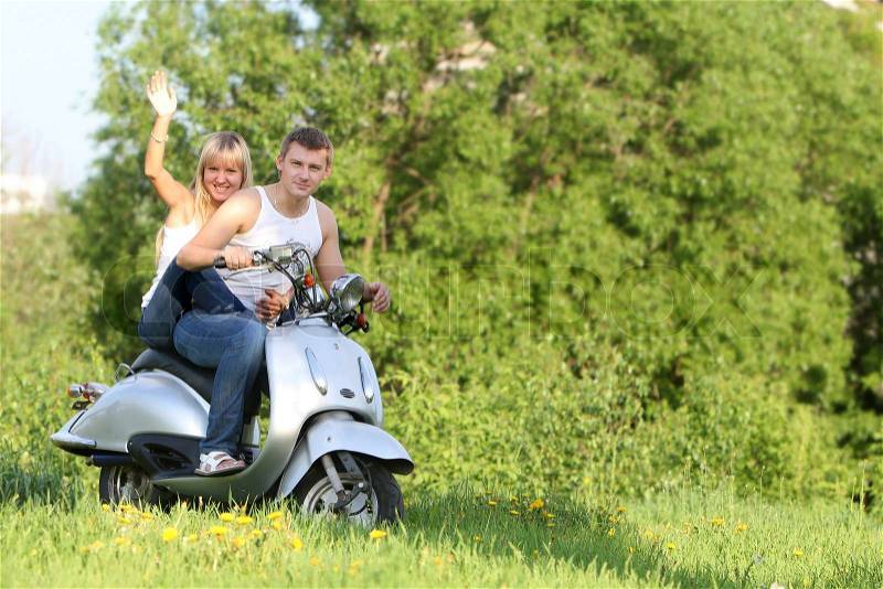 Young happy couple on motorbike / scooter on natural background, stock photo