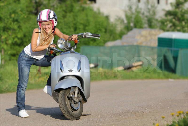 Portrait of young happy woman on motorbike / scooter outdoors, stock photo