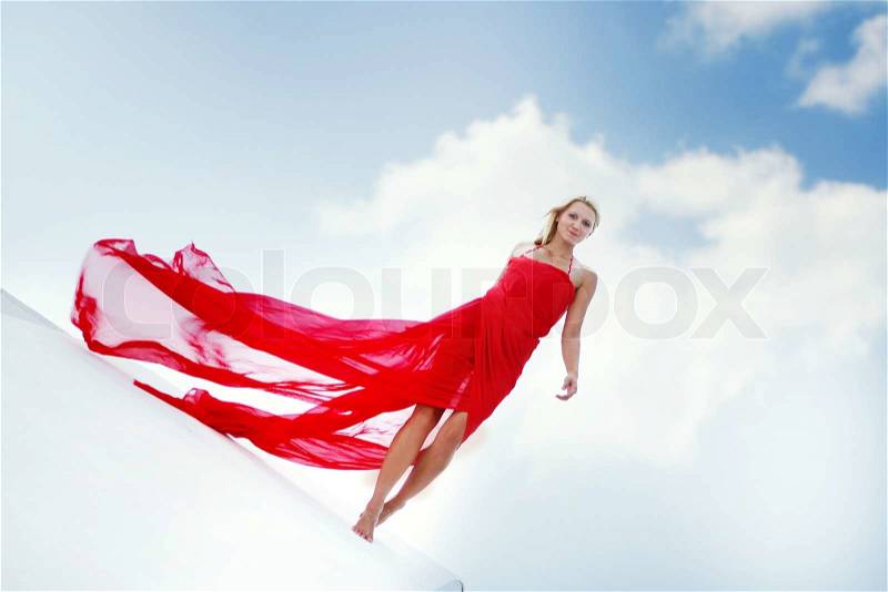 Outdoor portrait of young beautiful woman in long red dress walking over sky background, stock photo