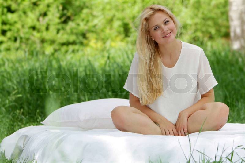 Young happy woman on white bed on natural background, stock photo