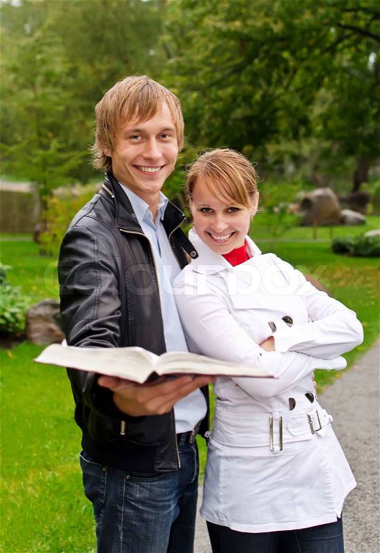 Two students with open book in the park, stock photo