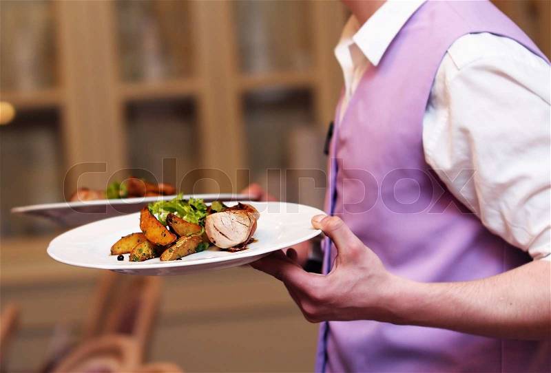Waiter carrying two plate with meat and baked potato, stock photo