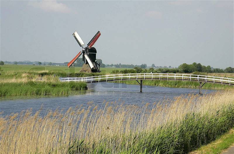 Dutch landscape with windmill canal and wooden bridge, stock photo