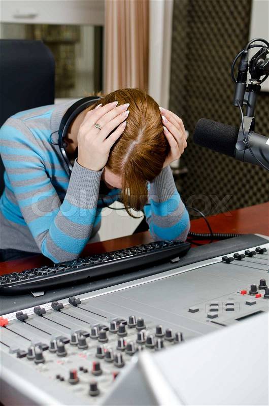 Portrait of depressed female dj working in front of a microphone on the radio, stock photo