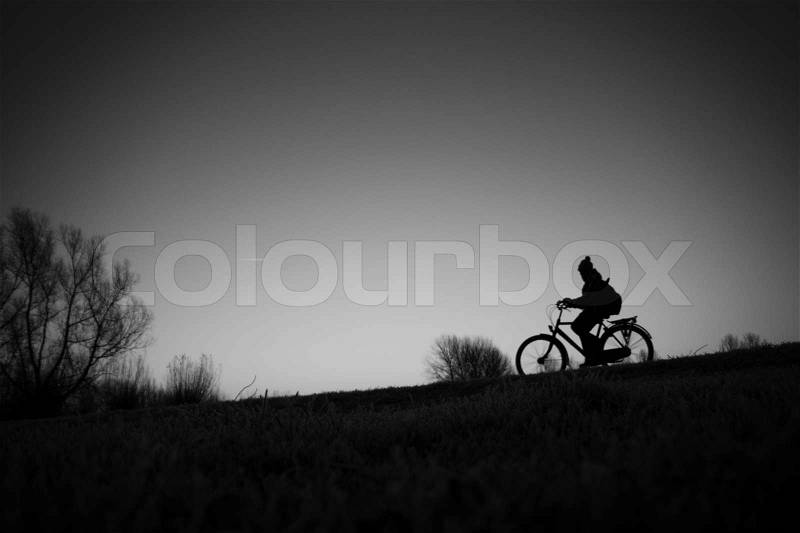 Solitary boy with cap is biking to school in fall in black and white, stock photo