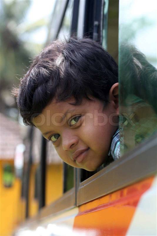 Handsome and cute little indian school kid looking back with happiness from the window of a school bus The face shows the innocence and childishness of the 6 year old boy with a smile on his face, stock photo