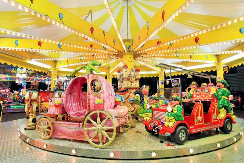 Round carousel with firefighter\'s car, coach and horses at Luna Park in Alba, Italy, stock photo