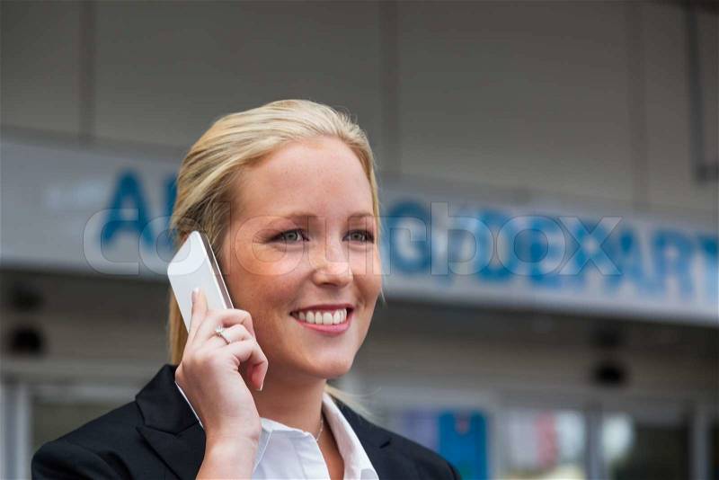 A business woman on the phone with her cell phone at the airport roaming charges on smartphones abroad, stock photo