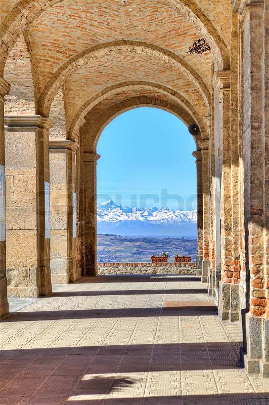 Vertical oriented image of ancient arch passage and snowy mountain peaks on background in town of Diano D\'Alba, Piedmont, Northern Italy, stock photo