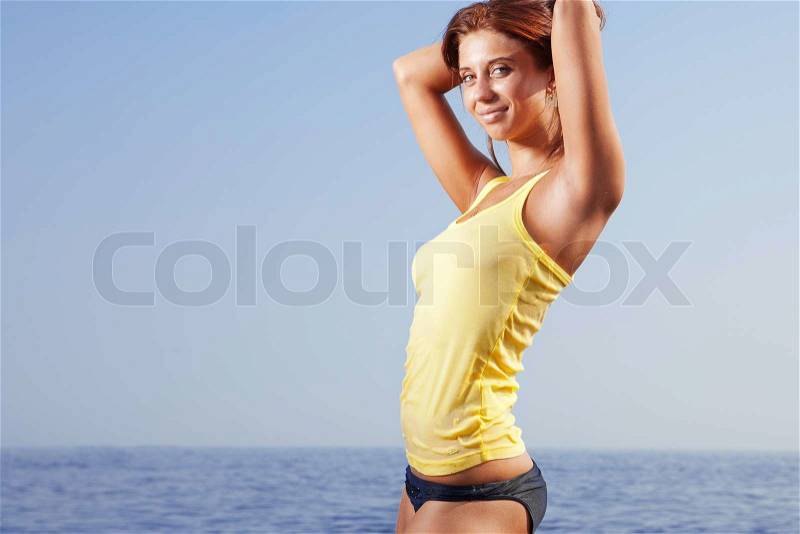 Sexy young woman in bikini standing by the sea with her wide open towards sky, stock photo