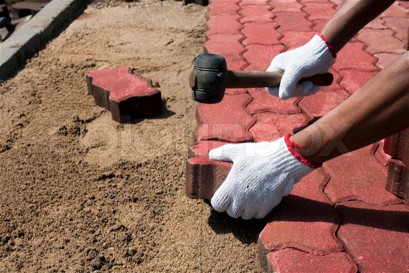 Aworker laying red concrete paving blocks, stock photo