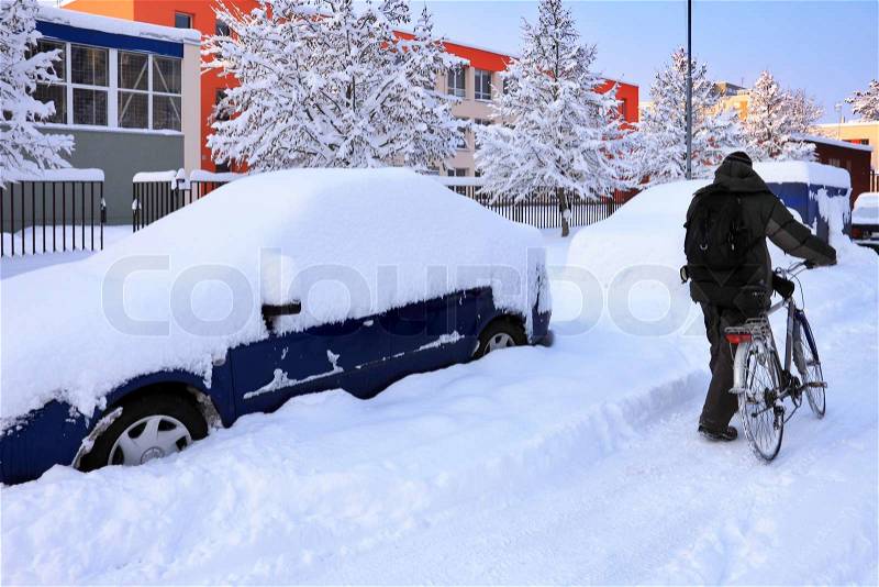 Snow-covered car lot in town with cyclist, stock photo