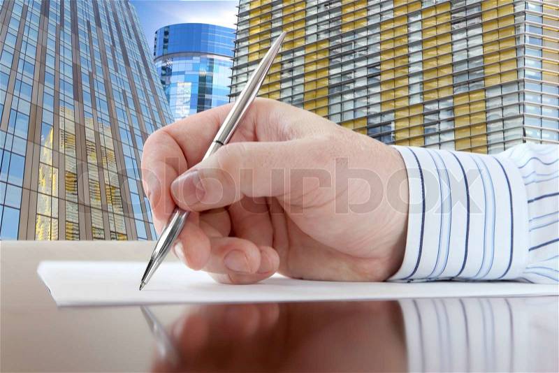 Businessman\'s Hand with Pen on the Office Buildings Background, stock photo