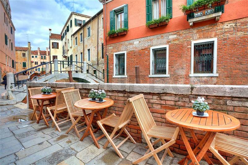 Wooden tables on narrow street among tipical colorful houses and small bridge in Venice, Italy, stock photo