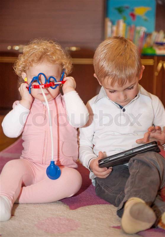 Brother with digital tablet, sister with toy medical kit, stock photo