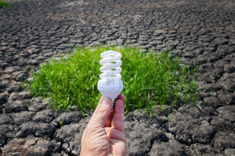 Energy saving lamp in hand over green grass and cracked earth, stock photo