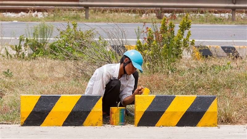 Man painting roadworks barriers on a road in Vietnam, stock photo
