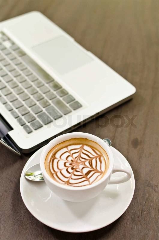 Coffee cup and laptop on the wood texture, selective focus on coffee cream, stock photo