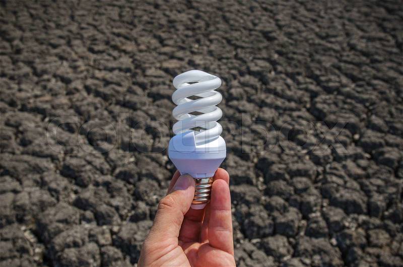 Energy saving lamp in hand over drought earth, stock photo