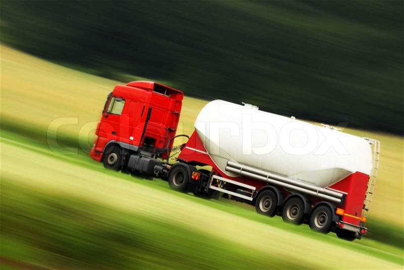 Large white cistern truck speeding on highway with blurred countryside panorama in background, stock photo