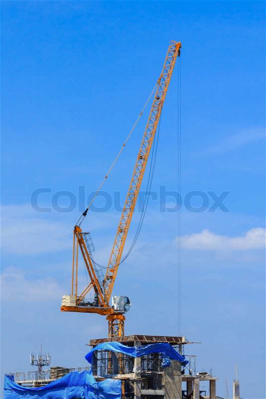 Yellow tower crane on building top with blue sky, stock photo