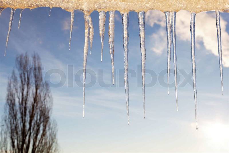 Icicles in the sunny day against a blue sky with white clouds, stock photo