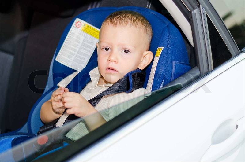 Little boy in a child safety seat sitting patiently in the back of a car, stock photo