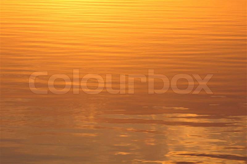 Ripples on the yellow water surface lit by the rising sun, stock photo