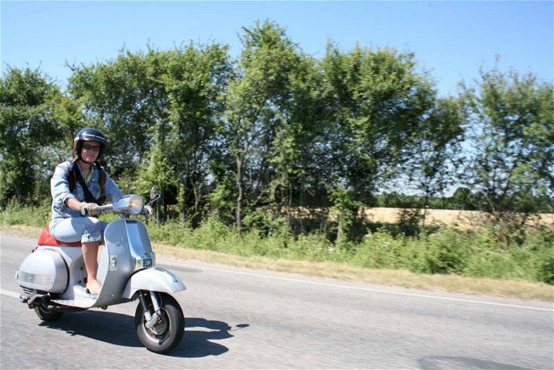 Young woman in helmet driving white scooter on road with line up trees, stock photo
