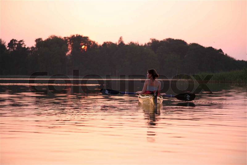 Woman swimming in kayak in lake during beautiful sunset, stock photo