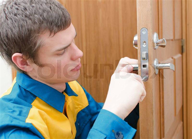 Young handyman in uniform changing door lock, stock photo