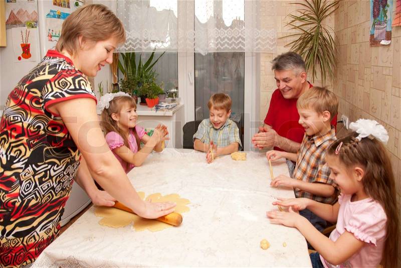 Happy big family cooking a pie together. Father, mother and four children, two boys and two girls playing with dough in the kitchen, stock photo