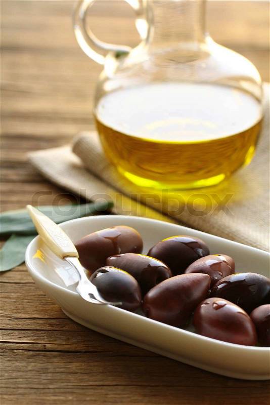 Natural organic olives in a white bowl, a bottle of oil in the background, stock photo
