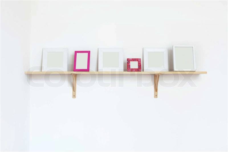 Simple blank photo frames on a shelf over white wall, stock photo