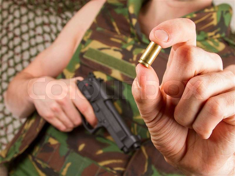Soldier in camouflage vest is holding a gun and an empty shell, stock photo