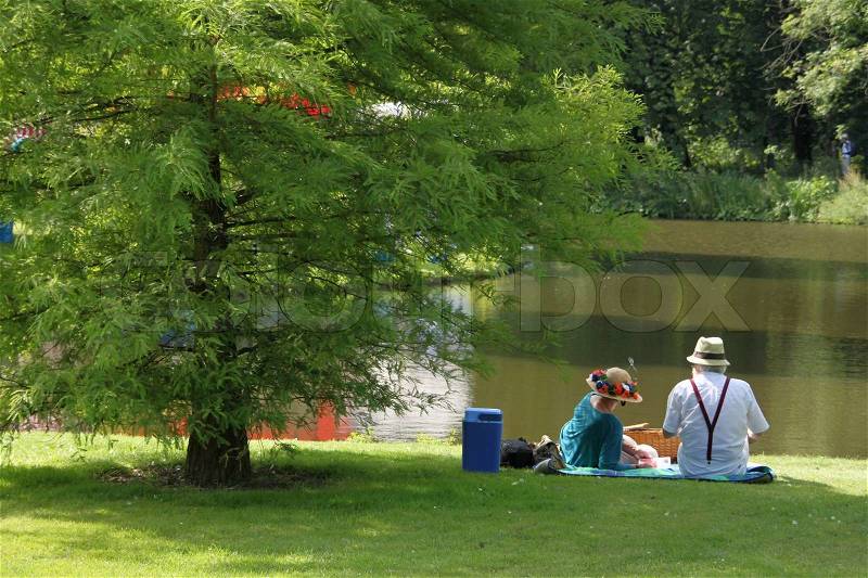 Under the tree, a happy couple dressed in old style and a blue cool box having fun and a wonderful view, stock photo