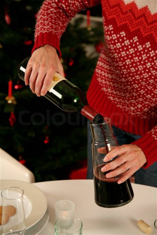 A woman pouring red wine in a decanter on Christmas table, stock photo