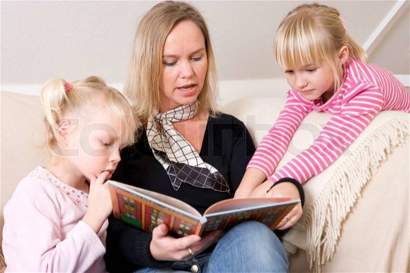 A caucasian mother reading a book to her daughters, stock photo
