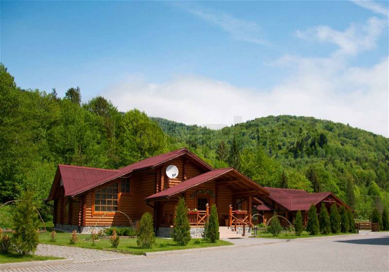 One modern wooden log cabin with all facilities in the mountains with many trees in the forest during spring time. Against blue sky, stock photo