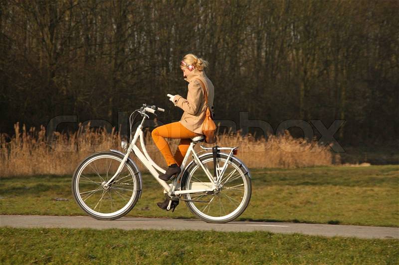 Going home from school, the girl dressed in colours of fall, with her white bike is cycling and always online, stock photo