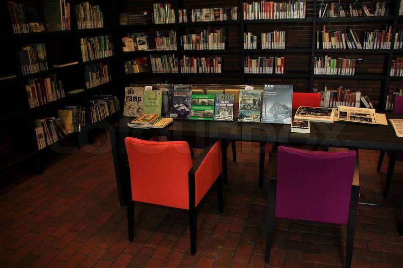 Room in municipal library with table and two chairs, orange and purple, with all kinds of books, stock photo
